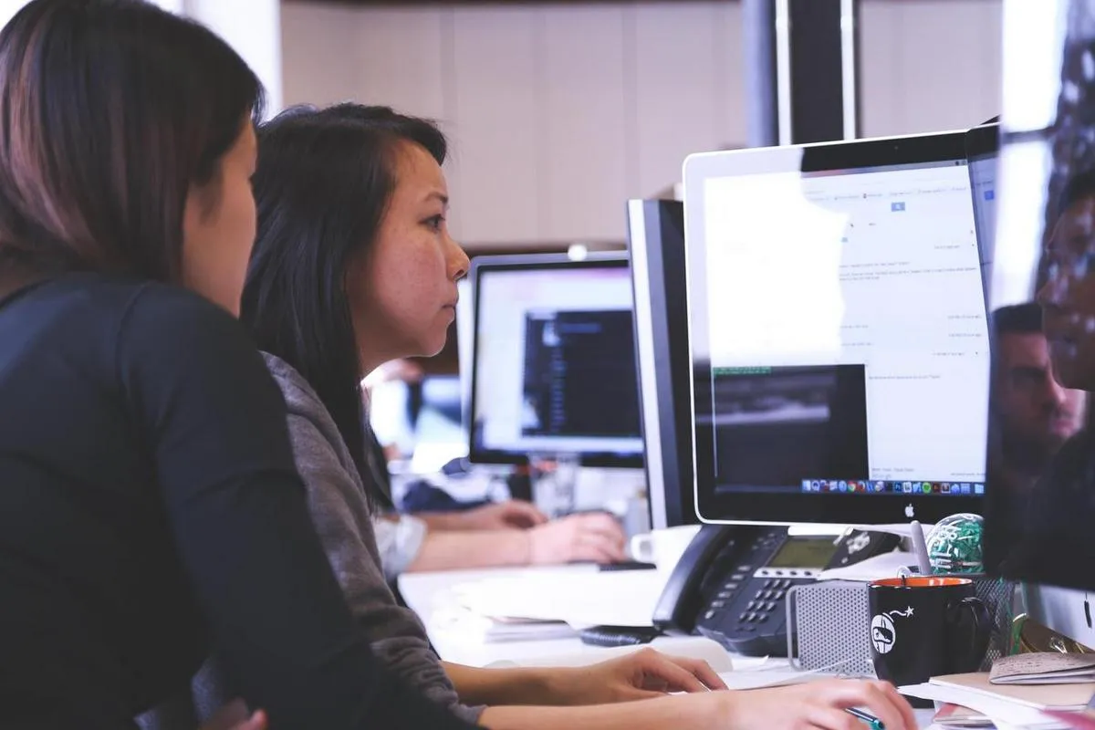 Two women at a desktop computer learning about digital signage cloud software options.