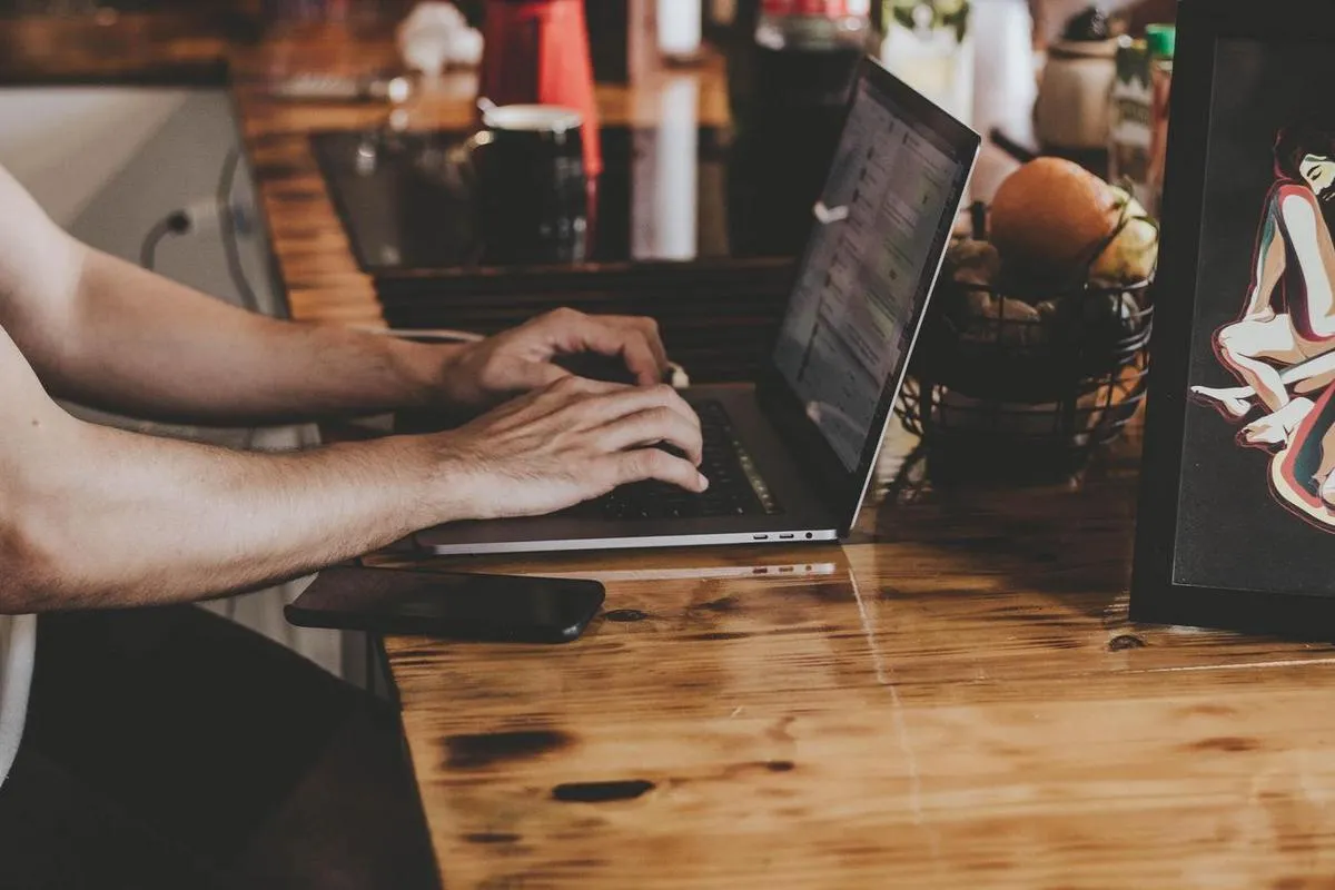 A man at a wooden desk choosing a digital signage platform using his laptop.