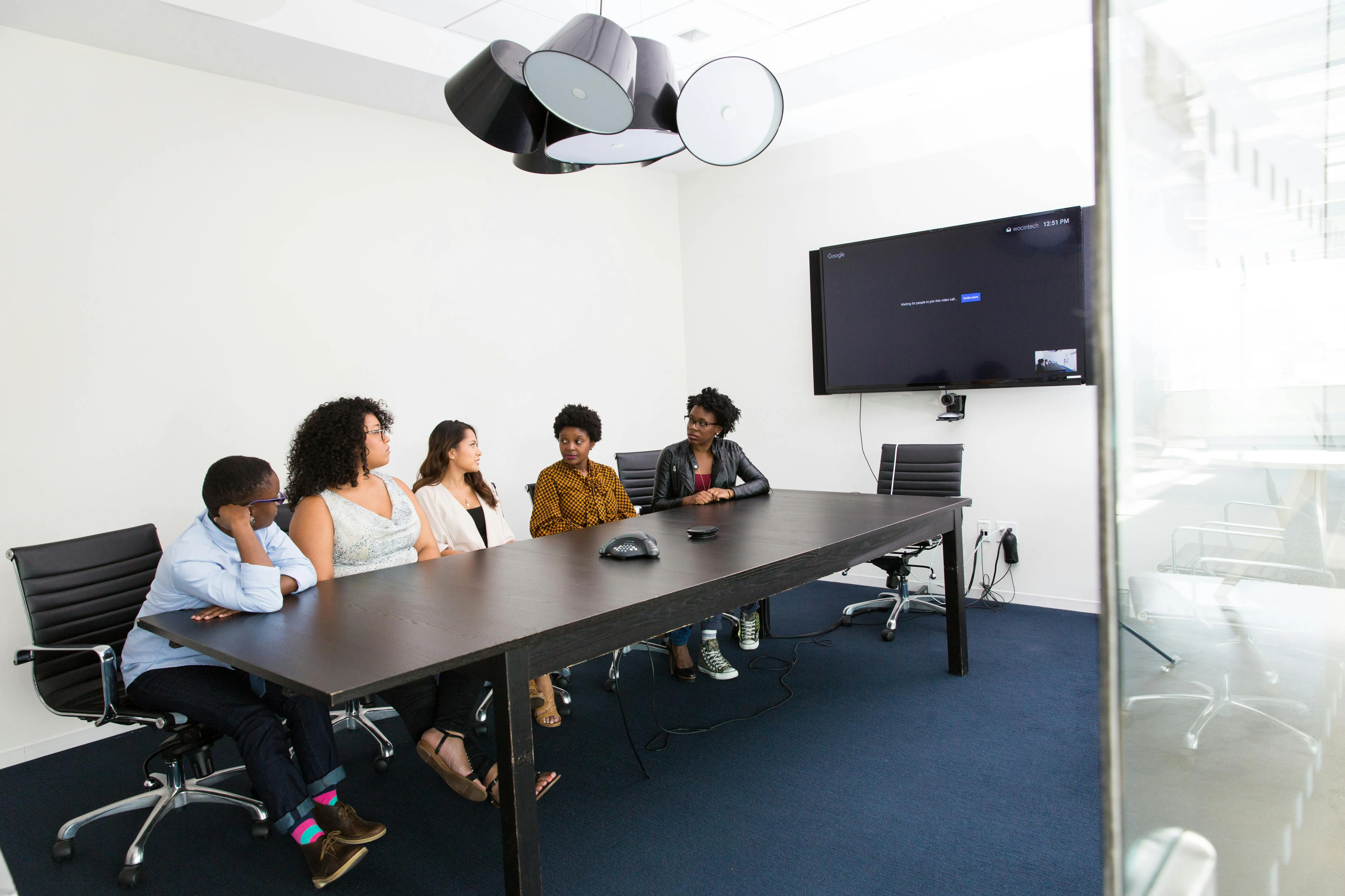 A meeting room filled with employees around a large table and a meeting room digital sign on the wall behind them.