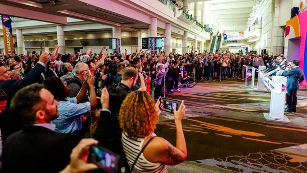 Busy opening day at InfoComm in Orlando, Florida. People on a carpet floor surounding the entrance in a brightly lit convention center.