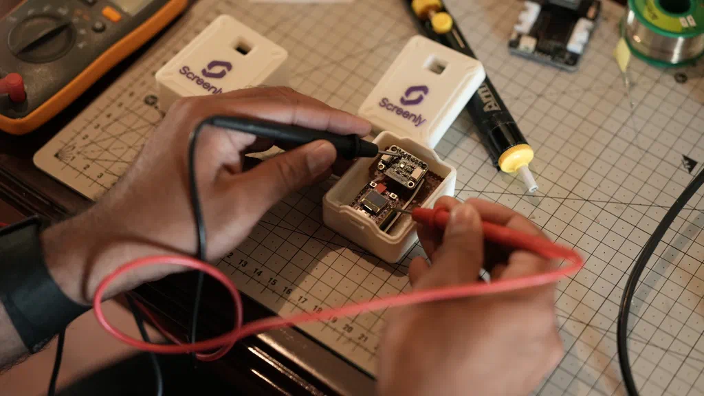 Testing a soldered PCB inside a Screenly-branded enclosure with a multimeter