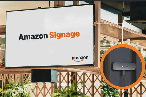 Amazon Signage Stick plugged into a wall-mounted screen displaying the Amazon Signage logo